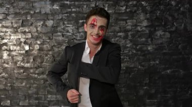 Gösterişli siyah takım elbiseli, karizmatik bir vampir adam dramatik bir siyah tuğla duvara karşı kartvizitini sunuyor. Göz alıcı makyajı, kan kırmızısı aksanları, Cadılar Bayramı ruhunu güçlendiriyor, bu görüntüyü ürkütücü hale getiriyor.