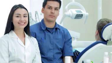 Parlak ve davetkar bir diş muayenehanesi, gülümseyen bir kadın stajyer ve kendinden emin bir erkek dişçinin yer aldığı yeni bir iş günü için zemin hazırlıyor. Birlikte profesyonellik ve samimiyet sergiliyorlar. Hasta bakımına bağlılıklarını gösteriyorlar.