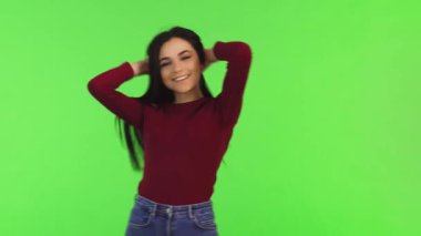 Uzun, dalgalı saçları olan neşeli genç bir kadın, parlak yeşil bir arka plana gülümserken bukle bukle saçlarını çeviriyor. Rahatlamış duruşu ve neşeli ifadesi gençlik güzelliğinin özünü yakalayarak kendine güven ve canlılık yayıyor.