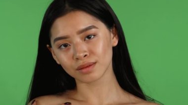 Çekici genç bir Asyalı kadın kameraya güvenle bakarken kusursuz tenine nazikçe dokunuyor. Işıl ışıl güzelliği, gençlik cazibesini arttıran renkli bir arka plan karşısında duran zarafet ve canlılığı yansıtıyor.