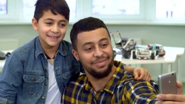 Çekici bir baba ve küçük oğlu keyifli bir anı paylaşıyorlar. Keyifli aletlerle çevrili, rahat bir masada selfie çekiyorlar. Gururlu Afrikalı Amerikalı baba sevinçle ışıldarken küçük oğlu kot ceket giyip elini dinlendiriyor.