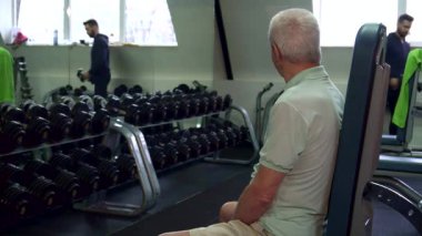 Genç bir Kafkasyalı antrenör spor yapmaya hazırlanan spor salonundaki yaşlı bir adama bir çift dambıl uzatıyor. Spor salonları ağırlık ve spor malzemeleriyle dolu canlı atmosfer, sağlığa olan bağlılığı vurguluyor ve