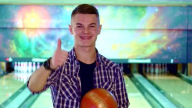 Şık saç kesimi ve gözlüklü neşeli beyaz bir adam elinde canlı kırmızı bir bowling topu tutarken başparmağını kaldırıyor. Bowling sahalarının ve lobutların rengarenk arkaplanlarına karşı kurulmuş, heyecanı yayılıyor, diğerlerini davet ediyor.