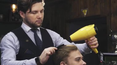 Dinamik bir çekim, bakımlı sakallı yakışıklı genç bir adamı yakalar. Yetenekli bir berberin saçını taramak için canlı sarı bir saç kurutma makinesi kullanması gibi gülümser. Bu sahne entelektüellik ve modern erkeksiliği yansıtıyor, berberliğin sanatını gözler önüne seriyor.