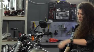 Çekici bir bayan motorcu, parlak bir helikopterin üstünde kıvırcık saçlarını bir anlık kaygısızca geriye savuruyor. Şık bir siyah deri ceket ve kot şort giyen bu çekici beyaz kadın cesur ve maceraperest bir kadın sergiliyor.