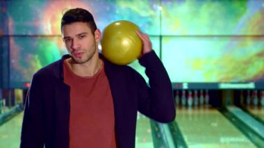 Çekici beyaz bir adam büyüleyici bir gülümseme ile omuzunda parlak sarı bir bowling topu dengeleyerek, önündeki şeride nişan almaya hazır. Kozmik arkaplan, bovling salonunun heyecanını arttırarak heyecan verici bir ortam yaratıyor.