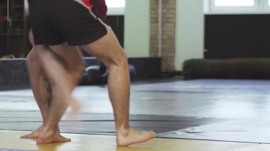 Odaklanmış bir erkek karma dövüş sanatları dövüşçüsü dinamik bir spor salonu ortamında antrenman partnerine ustalıkla kol kilidi takar. Sahne kararlılık ve güç saçıyor, idmanlarının yoğunluğunu ve yakalama sanatını gösteriyor.