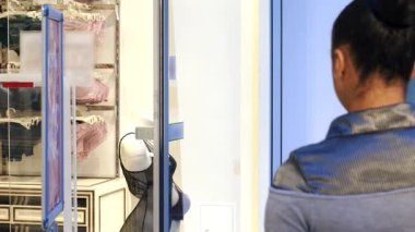 Güzel bir Afro-Amerikalı kadın parlak bir tebessümle arkasını dönüyor, şık bir iç çamaşırı mağazasının vitrininde alışveriş torbalarını gösteriyor. Bu şık esmer, kendine güven ve zarafet yayıyor. Şehir alışverişinin coşkulu ruhunu somutlaştırıyor.