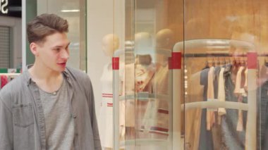 Yakışıklı bir genç adam modern bir butik vitrininde sergilenen şık kıyafetlere dikkatle bakar, moda ve stil dünyasını yansıtır. Alışverişin heyecanını yansıtan dışavurumcu tavrı, bir sonraki şık alışverişini yaparken...