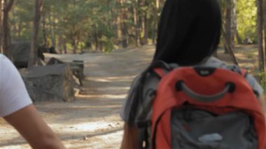 Neşeli bir çift, yükselen ağaçlar ve canlı yeşilliklerle çevrili güneşli patika boyunca el ele dolaşır. Çekici esmer kadın, sırt çantasıyla sakallı erkek arkadaşıyla neşeli bir gülümseme paylaşıyor.