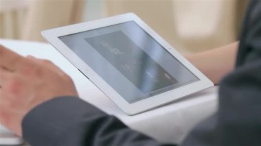 Yakından bakıldığında, genç, çekici bir işadamı ve iş kadınının elleri, dinamik bir tartışmada, parlak bir tabletteki verileri analiz ederken görülüyor. Sahne profesyonellik ve işbirliğini yayarak odaklanmış durumlarını vurguluyor