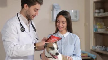 Dost canlısı bir erkek veteriner, her ikisi de sevimli bir köpeğe odaklanırken, ilgili dişi bir köpek sahibiyle hayati tedavi bilgilerini paylaşıyor. Beyaz önlük ve steteskop giymiş veteriner elinde kırmızı bir tedavi paketi tutarken, kadın sıcak bir gülümsemeyle...