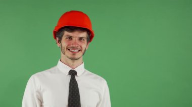 Parlak turuncu bir şapkası olan çekici genç bir erkek mühendis, canlı bir krom arka planda kameraya göz kırparken neşeyle ışıldıyor. Kendine güveni ve neşeli jesti inşaat endüstrisine coşku saçıyor.