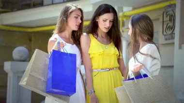 Her biri canlı alışveriş torbaları taşıyan üç neşeli kız moda mağazasının önünde heyecanlı bir anı paylaşıyorlar. Parlak gülümsemeleri ve eğlenceli etkileşimleri arkadaşlığın özünü ve birlikte alışveriş yapmanın neşesini yansıtıyor.