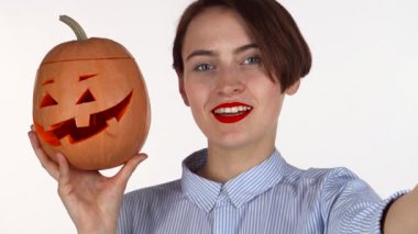 Kırmızı dudaklı neşeli genç bir kadın güzel oyulmuş Cadılar Bayramı balkabağıyla selfie çekerken anı yakalıyor. Bu canlı sahne neşe saçıyor, neşeli ruhunu ve bayramın ürkütücü çekiciliğini gösteriyor.