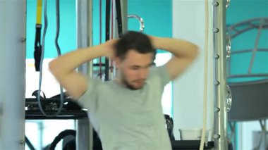 Orta Doğulu etnik kökenli odaklanmış genç bir adam hareketli bir spor salonunda sırt kaslarını ve omuz kemerini hedef alan dinamik bir esneme programına başlıyor. Parlak turkuaz arka plan enerji dolu atmosferi güçlendiriyor, kendini adamışlığını gösteriyor.