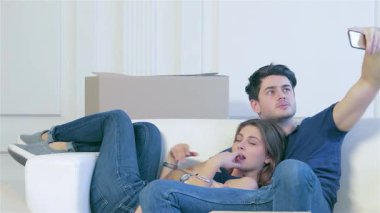 Neşeli bir çift, rahat beyaz bir kanepede bir araya toplanmış, hareket eden kutulardan oluşan bir denizin ortasında telefon kameralarına parlak bir şekilde gülümsüyor. Hayatlarındaki bu yeni bölüme adım attıklarında, neşeli ifadeleri sevgi ve heyecan saçıyor.