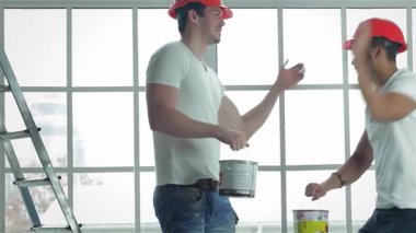 İki yetenekli işçi, biri boya kovası tutuyor, diğeri fırçayla, neşeli bir şekilde el sıkışıyor, parlak, boş bir dairede. Gülümsemeleri, pencereleri ölçerken memnuniyet saçıyor ve yenilenmeye hazırlanıyor.