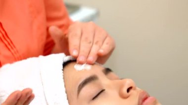 Yetenekli bir masör, sakin bir güzellik merkezinde genç bir Asyalı kadının huzurlu yüzüne nazikçe yatıştırıcı bir krem sürer. Bu lüks tedavi onu gençleştirici bir yüz masajına hazırlıyor, onu rahatlık ve ilgiye boğuyor.