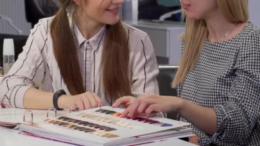 İki neşeli bayan arkadaş şık bir güzellik salonunda renkli bir saç boyası çizelgesini inceliyor. Işıl ışıl gülüşleri ve etkileyici sohbetleri, saç yoluyla arkadaşlığın ve kendini ifade etmenin sevincini gösteren canlı bir atmosfer yaratıyor.