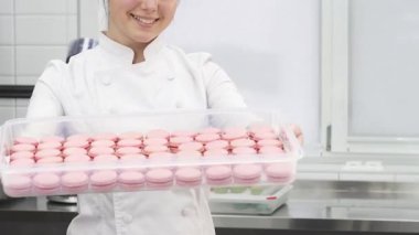 Neşeli bir kadın pasta şefi parlak, modern bir mutfakta şeffaf pembe badem kurabiyeleriyle dolu bir tepsiyi tutarken gururla ışıldıyor. Bu enfes sahne aşçılık sanatının özünü ve nefis bir zevk yaratma zevkini yansıtıyor.