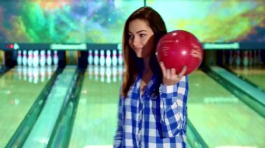 Esmer, çekici beyaz bir kız canlı kırmızı bir bowling topunu kendinden emin bir şekilde beşik gibi sallıyor. Arkaplanda parıldayan şeritlere neşe saçıyor. Şık, kareli bir gömlek giyip, neşeli bir poz veriyor, bowling salonunun heyecanını somutlaştırıyor.