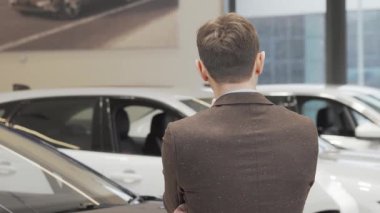Şık bir takım elbise giymiş neşeli, olgun bir adam, arabasını alırken kameraya gülümsüyor. Çağdaş bir galeride parıldayan araçlarla çevrelenmiş, mükemmel bir araba bulmanın heyecanını yaşıyor.