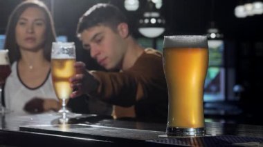 Genç bir çift coşkulu bir barda kutlama yaparken, ön planda ferahlatıcı bir bardak altın bira belirgin bir şekilde duruyor. Bu canlı sahne aşkın ve yoldaşlığın özünü yakalıyor, şenlikli bir gece için mükemmel.