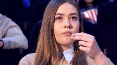 Uzun kahverengi saçlı, güzel beyaz bir kızın çarpıcı yakın çekimi yoğun bir film izlerken derin endişelerini açığa çıkarıyor. Etrafı karanlık bir tiyatroyla çevrili, geniş gözleri ekrandaki dramı yansıtıyor.