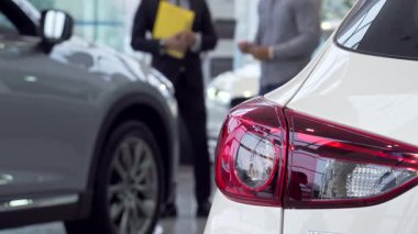 İyi giyimli bir satıcı potansiyel bir alıcıyla seçenekleri tutkuyla tartışırken, modern arabaların çarpıcı bir yakın çekimi arka planda. Bu dinamik sahne yeni bir araç seçmenin heyecanını yakalıyor.