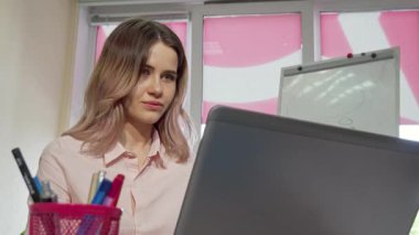 Canlı bir üniversite öğrencisi kameraya ışıldıyor. Çalışmalarına parlak bir dizüstü bilgisayarla dalmış. Bu canlı sahne, renkli kırtasiye ve parlak çalışma alanı ile çevrili mezuniyet sınavlarına hazırlanırken onun kararlılığını ve neşesini yansıtıyor.