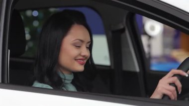 Neşeli genç bir kadın yeni arabasının anahtarını elinde tutarken gururla ışıldıyor, canlı bir galeri galerisinde heyecanını sergiliyor. Arkasındaki parlak araç modern otomotiv teknolojisini yansıtıyor, başarıyı ve heyecanı simgeliyor.