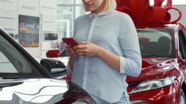 Açık mavi bluzlu neşeli bir kadın akıllı telefonuna yazarken gülümsüyor, modern bir bayilikte parıldayan otomobillerle çevrili. Bu canlı sahne bir araç satın almanın heyecanını yakalıyor, teknolojiyi araba heyecanıyla harmanlıyor.
