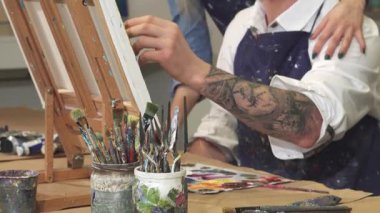 Çekici dövmeli bir sanatçı tuval üzerine tutkuyla resim yaparken güzel kız arkadaşı arkasından ona sevgiyle sarılıyor ve mutluluk ve destek veriyor. Bu iç açıcı sahne yaratıcılığın ve romantizmin özünü yansıtıyor.