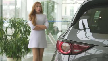 Şık elbiseli çarpıcı bir kadın modern bir araba galerisinde dalgın dalgın duruyor, bakışları parlak bir araca sabitlenmiş. Doğal ışıkla dolu parlak sergi salonu, karar verme anının cazibesini arttırıyor, güzelliği tüketimcilikle harmanlıyor.