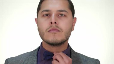 Takım elbiseli şık bir adam papyonunu düzeltir, saf beyaz bir arka plana karşı kendine güveni ve çekiciliği yayar. Sıcak gülüşü ve dengeli tavırları profesyonelliğin ve tarzın özünü yansıtıyor ve bu imajı iş ilişkisi için mükemmel kılıyor.