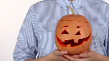 Genç bir kadın, Cadılar Bayramı geleneklerine olan sevgisini göstermek için oyulmuş bir balkabağı fenerini nazikçe okşuyor. Canlı turuncu balkabağı, neşeli sırıtışıyla, beyaz bir arka plana karşı duruyor, neşe ve şenlik ruhunu çağrıştırıyor.