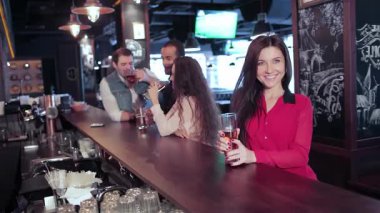 Canlı kırmızı tişörtlü bir kız bira bardağını kaldırıyor ve arkadaşlarını hareketli bir barda kutlamaya davet ediyor. Kahkahalar ve tezahüratlar havayı doldururken, arkadaşlarla içkinin keyfini çıkarırken ve tutkulu bir şekilde desteklerken atmosfer heyecan vericidir.