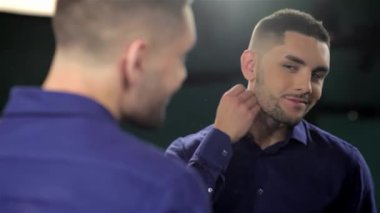 Şık bir berber dükkanında, kendine güvenen bir adam yansımasına bakarken bakımlı sakalını okşar. Sahne, modern erkeksiliğin özünü yakalıyor, kuaförlüğün sanatsallığını ve kendine bakmanın özel atmosferini gözler önüne seriyor.