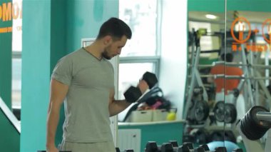 Ortadoğu kökenli kararlı bir genç adam, aynada vücudunu incelerken dambıllarını kaldırarak güçlü bir antrenman yapıyor. Zindelik ekipmanlarıyla dolu canlı spor salonu, kendini adamışlık atmosferini yükseltir ve...