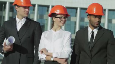 Üç kendine güvenen şık takım elbiseli ve parlak turuncu kasklı mimar hareketli bir inşaat sahasında bir araya gelerek iddialı projelerini gözden geçiriyorlar. Dengeli tavırları ve takım çalışmaları yenilikçi bir tasarıma ve başarıya olan bağlılıklarını yansıtıyor.