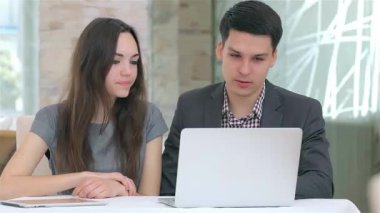 Genç, çekici bir iş adamı ve kadın, modern bir ofis ortamında düzgün bir dizüstü bilgisayardaki verileri analiz ederek odaklanmış bir tartışmaya girişiyor. Bir fincan kahve içerken, ifadeleri işbirliği ve coşkuyu yansıtıyor.