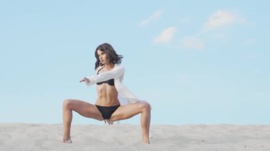 Çarpıcı bir kadın dansçı, geniş bir çöl manzarasının önünde esnekliğini ve sanatını sergiliyor. Altındaki sıcak kum ve yukarıdaki parlak mavi gökyüzüyle kendine güveni ve kadınlığı somutlaştırarak büyüleyici bir performans sergiliyor.