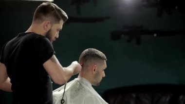 Modayı takip eden bir berber dükkanında yetenekli bir berber genç bir adamın saçını modern saç kesimi için makas kullanır. Atmosfer canlı ve erkeksi, arka planda klasik dekor ve hafif ışıklandırma ile tımar deneyimini güçlendiriyor.