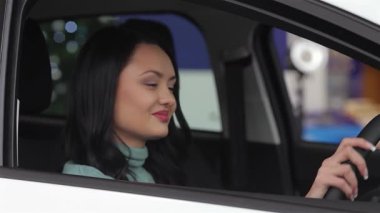 Neşeli bir gülüşü olan kendine güvenen genç bir kadın modern bir bayilik ortamında heyecanını sergiliyor. Gösterişli araçlarla dolu sergi salonunun canlı atmosferi, önemli bir alışveriş yapmanın verdiği keyfi vurguluyor.