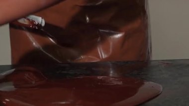 Gösterişli bir önlük ve eldivenle kaplanmış, odaklanmış bir çikolata ustalıkla cilalı bir tezgahın üzerinde lezzetli sıcak çikolatayı ısıtarak ev yapımı şekerlemelerin başyapıtını oluşturuyor. Bu canlı sahne sanattaki ustalığı ve hassasiyeti yansıtıyor.