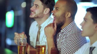 Canlı bir barda heyecanlı bir futbol maçı izlerken tutkuyla tezahürat yapıp bağıran, şık giyinmiş üç hevesli arkadaş. Neşeli arkadaşlıkları bira bardaklarını tokuşturup heyecan verici bir şey yaratarak ön plana çıkıyor.