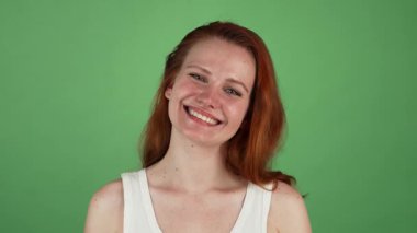 Genç, neşeli bir kadın, neşeyle saçlarını dalgalandırıyor, başarılarını kutlamak için yumruklarını sallıyor. Bulaşıcı gülüşü ve parlak tavırları yeşil renkli arka plana karşı canlandırıcı bir atmosfer yaratıyor.