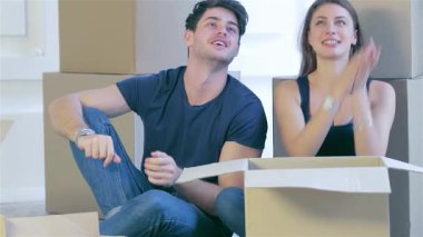 Neşeli bir çift, karton kutularla çevrili, boş dairelerinin zemininde oturuyor, neşeyle yeni dairelerinin anahtarlarını tutuyorlar. Gülüşleri mutluluğu kucaklarken, yeni başlangıçların heyecanını ve sıcaklığı yakalıyor.