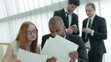 Kendine güvenen dört işadamı ve işkadınından oluşan odaklanmış bir grup, doğal ışıkla çevrili şık bir ofis masasında stratejileri aktif olarak tartışıyor. Belgeleri analiz ettikleri ve paylaştıkları için, bu etkileyici konuşmaları takım çalışmasını ve hırslarını yansıtıyor.